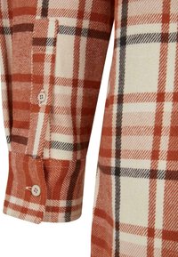 Hedvábná tkanina v červeno-bežovém kostičkovaném vzoru se zapínacími manžetami a kontrastními černými linkami, vyznačující se jemnou texturou a tkanými vzorovými detaily.