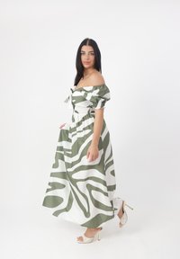 Abito lungo con maniche a spalle scoperte in un motivo astratto verde e bianco, con vita smock e tessuto fluido. Tacchi trasparenti.
