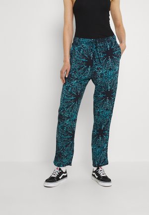 Woman wearing black tank top, loose navy blue pants with turquoise abstract pattern, white socks, and black sneakers with white laces.