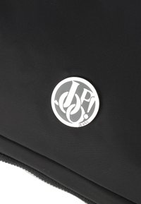 Borsa di stoffa nera con un logo circolare argentato che presenta il testo "JP!" e "JEANS". La superficie ha un aspetto intrecciato e testurizzato.