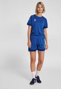 Niebieski strój sportowy składający się z koszulki z krótkim rękawem i spodenek. Materiał jest oddychający, o gładkiej fakturze i z akcentami logo.