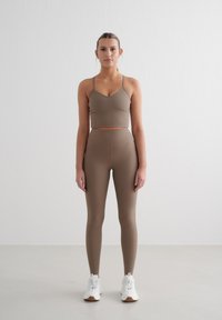 Un crop top côtelé marron et un legging taille haute assorti. La tenue présente un design ajusté avec des bretelles spaghetti, accompagnée de baskets blanches.