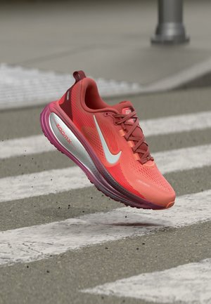 Κόκκινο και μωβ αθλητικό παπούτσι Nike σε ανοιχτό χώρο πάνω από διαβάση πεζών, με έμφαση στη λευκή σήμανση Swoosh και την απορροφητική σόλα ZoomX.