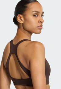 Sutien sportiv maro cu un design racerback și detalii tăiate, textură netedă și siluetă ajustată. Potrivit pentru îmbrăcăminte sportivă.