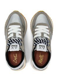 Zapatillas grises y plateadas con un diseño de materiales mixtos, cordones blancos, acentos a rayas en blanco y negro, y suela de goma clara.