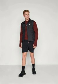 Melnā kvadrātveida veste virs bordo garām piedurknēm krekla, kopā ar melnām šortiem. Akcentēta ar logotipu un aukliņas detaļām. Melnas sporta kedas.