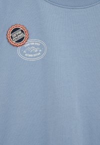 Világoskék szövet fehér ovális logóval, rajta a "Cedar Fork River Outdoor Division" felirattal és egy kerek folttal, amelyen a "Certified Explorers" szöveg olvasható.