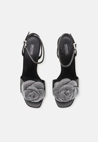 Sorte høyhælte sandaler med justerbar stropp, dekorert med en rose-design prydet med rhinestones foran og en glatt lærfinish.