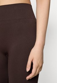 Brune ribbede leggins med høy livlinje. Teksturen er glatt med en svak stretchy følelse som gir en tettsittende silhuett.