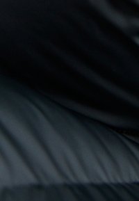 Czarna kurtka puchowa o gładkiej, pikowanej fakturze i podłużnych wzorach. Posiada zamek błyskawiczny z boku, tworzący elegancką sylwetkę.