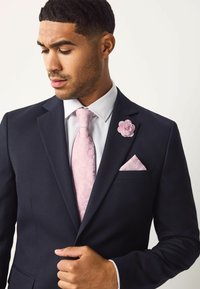 Tengerészkék szövetből készült öltöny, fehér ing, világos rózsaszín mintás nyakkendő, rózsaszín virág kitűző a galléron, és hozzáillő zsebkendő.
