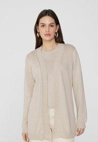 Beige Strickjacke mit offener Vorderseite, geripptem Saum und langen Ärmeln, über einem passenden Oberteil getragen, das eine glatte Textur und ein minimales Design aufweist.