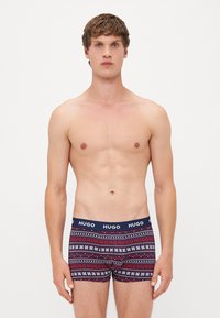 Marineblaue Boxershorts mit roten und weißen geometrischen Mustern. Der elastische Bund ist mit dem wiederholten "HUGO"-Label versehen. Aus Baumwollmaterial.