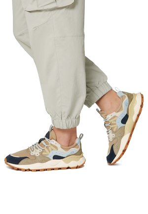 Beige und marineblaue Sneaker mit strukturiertem Obermaterial und gepolstertem Zungenbereich. Dicken weiße Sohle mit Gummilaufsohle. Akzente umfassen hellblaue und graue Details.