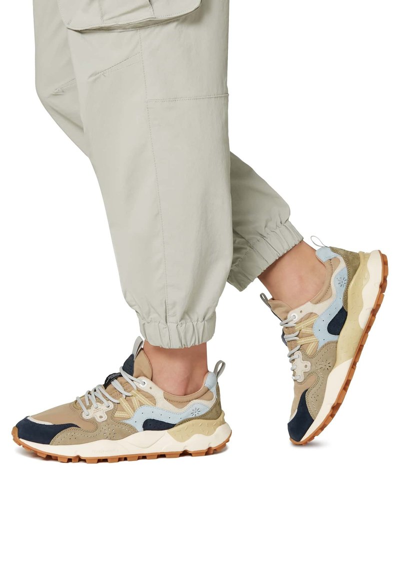 Béžové a námořnické tenisky s texturovaným svrškem a polstrovaným jazykem. Silná bílá podrážka s gumovým vzorem. Akcenty zahrnují světle modré a šedé detaily.