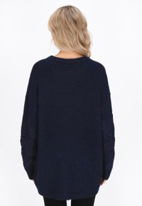 Laine oversize navy con un tessuto testurizzato, caratterizzato da un ricamo a spirale intricato sulle maniche lunghe e un semplice scollo rotondo.