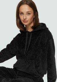 Zwarte corduroy hoodie met een voorzak, trekkoord capuchon en zachte textuur. Het ontwerp heeft een losse pasvorm en een ribpatroon.