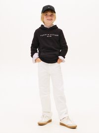 Melnā kapuce ar "TOMMY HILFIGER" logo, baltas bikses, baltas sporta kurpes un melna cepure ar logo detaļām. Nav fona elementu.