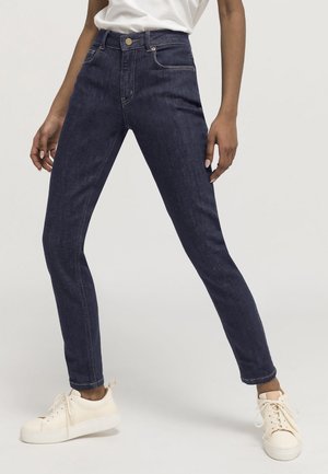 Jeans skinny a vita alta di colore blu scuro realizzati in denim. Presentano tasche frontali e posteriori, passanti per cintura e una chiusura con bottone dorato.