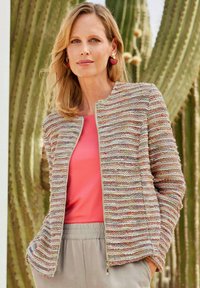 Giacca in tweed multicolore caratterizzata da una superficie testurizzata, scollatura rotonda e chiusura con zip, abbinata a un top corallo e pantaloni beige.