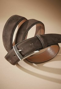 Brun ruskindsbælte med en sølvmetalknap. Har en glat overflade og flere huller til justering, hvilket viser et strømlinet design.