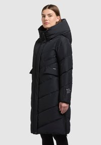 Must puffer-jope kõrge kraega, horisontaalse tikandiga, lukuga rinnatasku, küljetaskute ja varruka logoga.