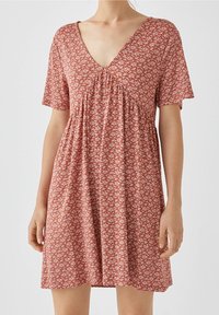 Kurzärmliges Kleid in Rostfarbe mit weißem Blumenmuster, ausgestattet mit einem V-Ausschnitt und gerafften Details unter der Brust. Leichtes Material.