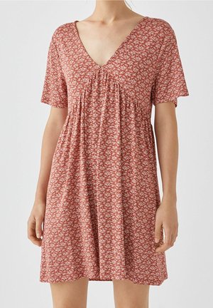 Robe à manches courtes de couleur rouille avec un motif floral blanc, présentant un décolleté en V et des détails froncés sous la poitrine. Tissu léger.