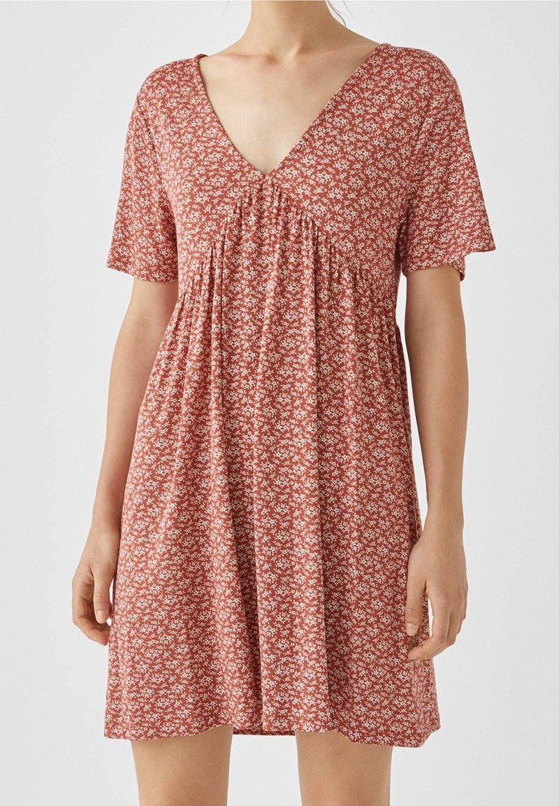 Kurzärmliges Kleid in Rostfarbe mit weißem Blumenmuster, ausgestattet mit einem V-Ausschnitt und gerafften Details unter der Brust. Leichtes Material.