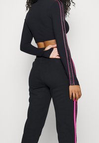 Musta urheiluasu, jossa on lyhyt hihainen paita ja korkea vyötärö, jossa on vaaleanpunaiset sivuviivat ja sileä, joustava pinta.