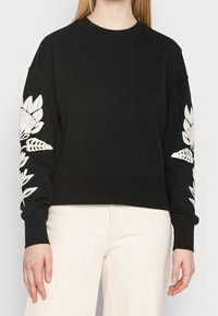 Czarny sweatshirt z długimi rękawami, z białym haftem kwiatowym na obu rękawach. Wykonany z miękkiego materiału, o luźnym kroju.