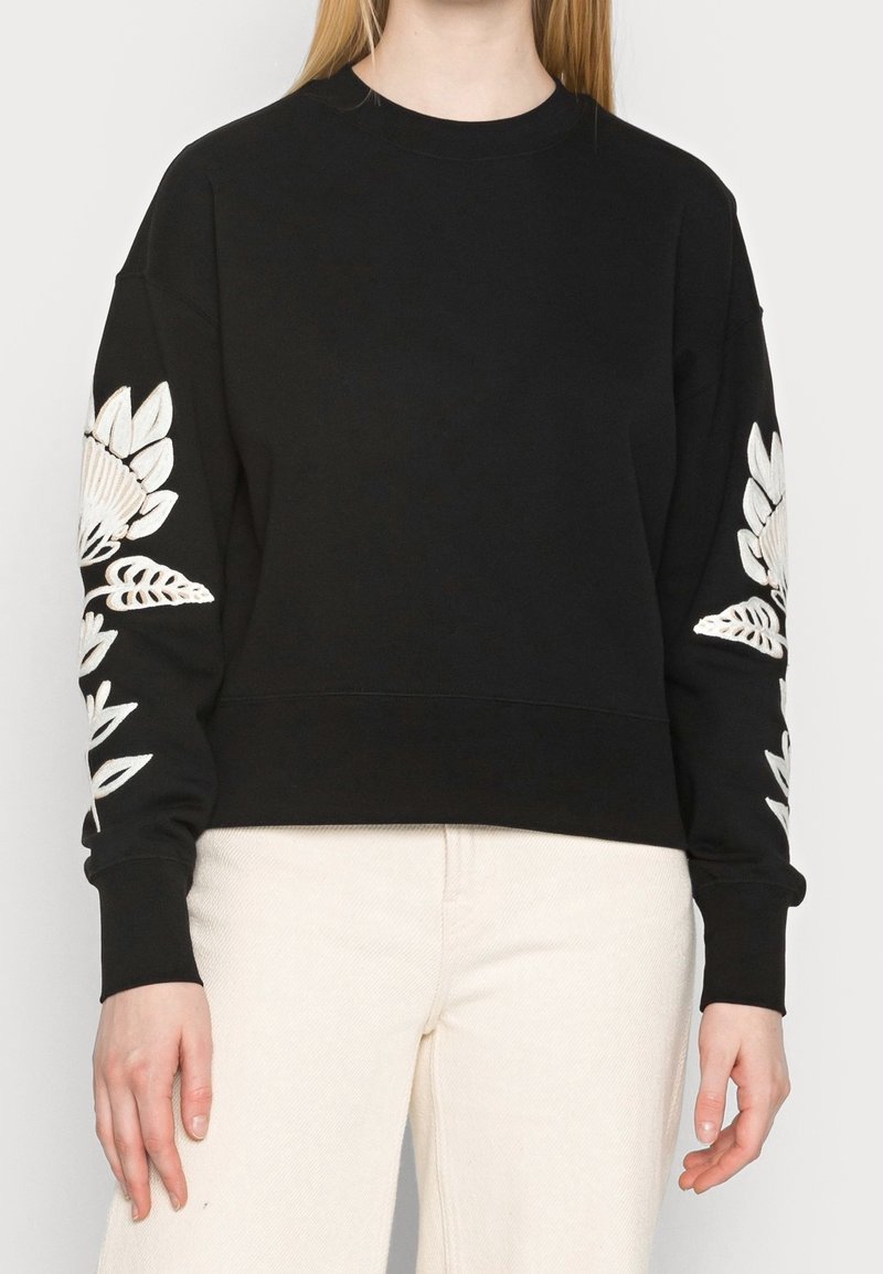 Czarny sweatshirt z długimi rękawami, z białym haftem kwiatowym na obu rękawach. Wykonany z miękkiego materiału, o luźnym kroju.