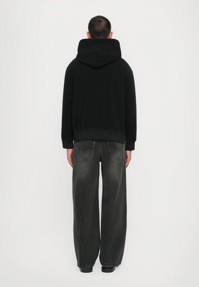 Svart hoodie med en stor bakficka och ribbade ärmmuddar, kombinerad med löst sittande grå jeans med bakfickor och sömdetaljer.