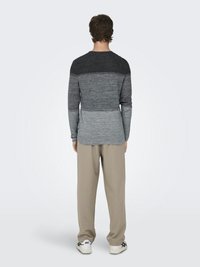 Top de punto de manga larga con un degradado de tonos gris oscuro a claro, combinado con pantalones beige y zapatillas blancas. Textura suave, diseño ajustado.