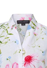 Weißes Hemd mit Kragen, das mit einem floralen Muster in Rosa, Blau und Grün verziert ist. Hergestellt aus leichtem Stoff, mit Knöpfen und einem Etikett, das die Größe 36 zeigt.
