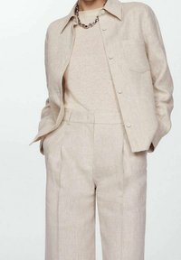 Veste en lin beige avec un col pointu, une poche avant et un pantalon taille haute assorti. Texture lisse avec de subtils lignes verticales.