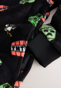 Black fleece fabric featuring various colorful cartoon character patterns. Includes a black ribbed cuff detail. Soft texture.