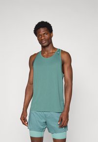 Green athletic tank top with a round neckline and racerback design, paired with matching shorts featuring a color-blocked hem and logo detail.