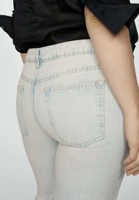 Jeans de mezclilla de lavado claro con un diseño ajustado, que presentan bolsillos traseros y detalles de costura sutiles, vistos de lado.