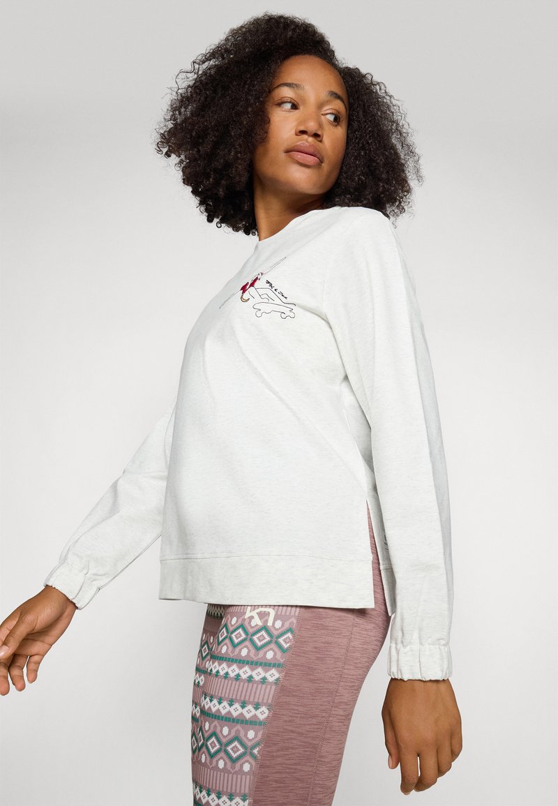 Helle graue langärmlige Sweatshirt mit Rundhalsausschnitt und gesticktem Design. Ein Paar gemusterte Leggings mit lila und türkisfarbenen Akzenten.