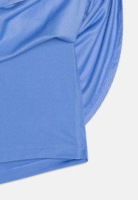 Närbild av blå sporttyg som visar släta och texturerade stickade sektioner med detaljerad sömnad på en rundad plaggkant.