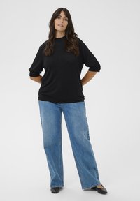 Czarny sweter z okrągłym dekoltem i lekko bufkami, połączony z jasnoniebieskimi dżinsami o szerokich nogawkach i czarnymi balerinami.