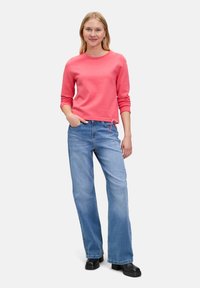 Top a maniche lunghe color corallo con texture a costine e dettagli con cordoncino, abbinato a jeans a gamba larga blu chiaro e scarpe con piattaforma nere.