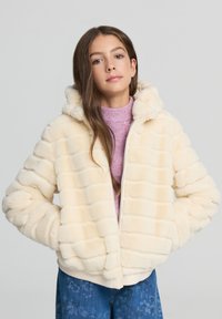 Kremowa puchowa kurtka z kapturem, z fakturowanym, prążkowanym wzorem. Nosi się ją na jasnoróżowym, prążkowanym swetrze.