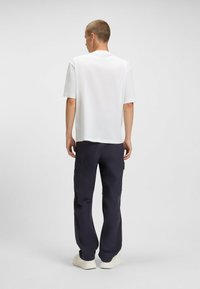 White short-sleeve T-shirt paired with navy cargo pants. T-shirt has a relaxed fit; pants feature side pockets and a straight cut. White sneakers.