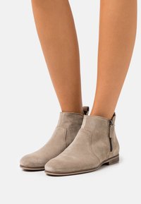 Bottes cheville en daim beige avec un petit talon empilé, une fermeture éclair latérale et un design minimaliste, avec des bouts arrondis et une texture lisse.