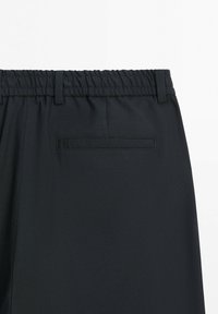 Set bagfra af sorte bukser med elastisk taljebånd, bæltestropper og en enkelt vandret baglomme.