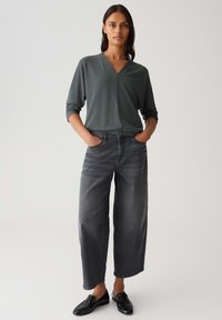 Maglione grigio morbido con scollo a V, abbinato a jeans grigi scuri a vita alta e a gamba larga. Mocassini neri completano l'outfit.