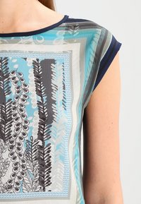 Short-sleeve top featuring a geometric pattern in shades of blue, gray, and black, with a lightweight, smooth texture.