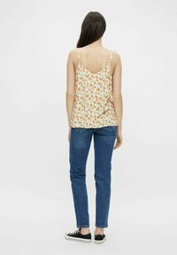 Blommig linne med spagettiband i ljusorange med gröna detaljer, parat med blå denimjeans. Svarta sneakers fulländar looken.